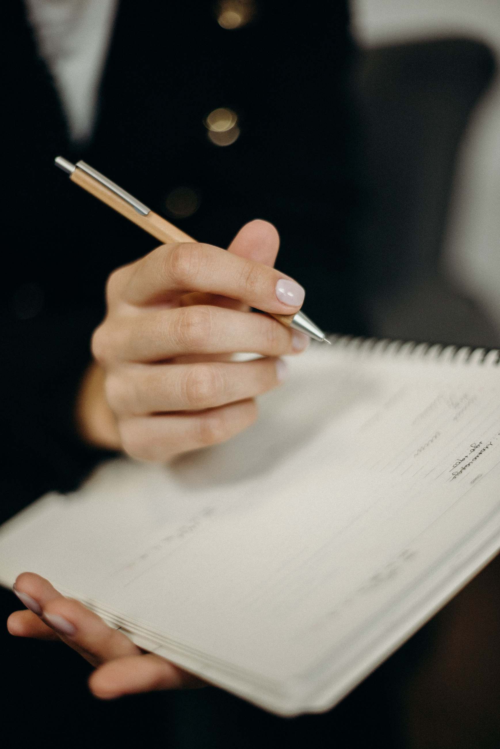 Hand, die mit einem Kugelschreiber Notizen in ein spiralgebundenes Notizbuch schreibt